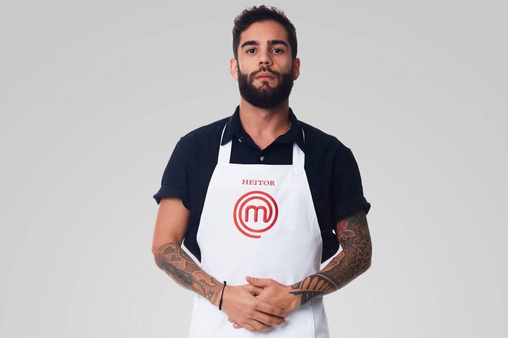 Homem de camisa de manga curta, avental do masterchef e mãos dadas sério