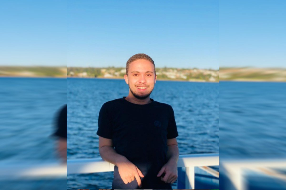 Imagem colorida de homem com camisa preto, com um lago no fundo