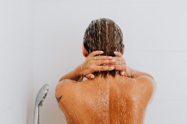 Color photo of a person bathing in a shower.back to camera bath