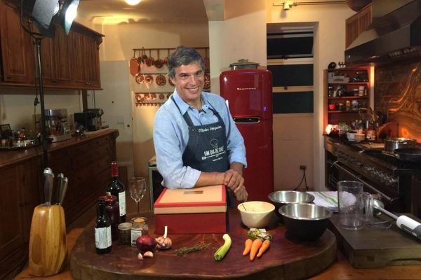 Chef Olivier Anquier apoia um braço em cima de uma caixa sobre mesa com ingredientes e utensilios