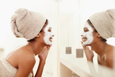 mulher negra em frente ao espelho com creme facial