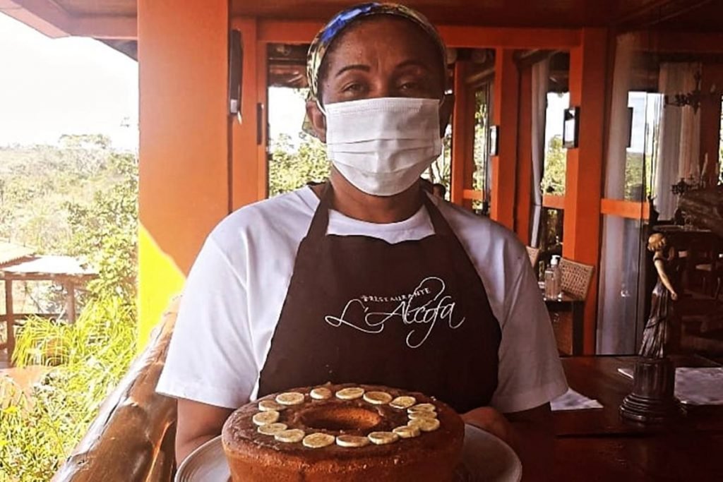 Dona Ana com máscara, avental e bolo na mão