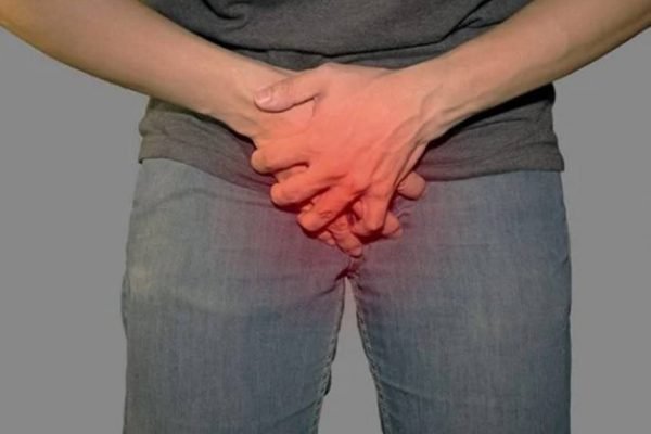 Homem vestido segura região do pênis e um efeito vermelho é aplicado como se inflamasse - Metrópoles