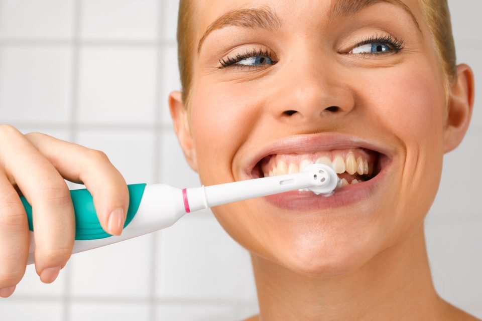 Fotografia colorida de mulher escovando os dentes com escova dental elétrica