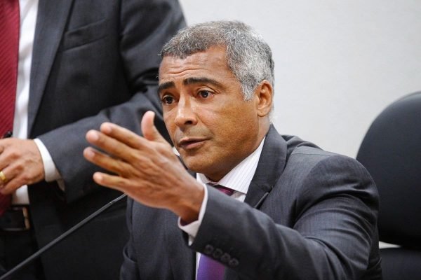 Senador Romário, de terno e gravata, fala ao microfone - Metrópoles