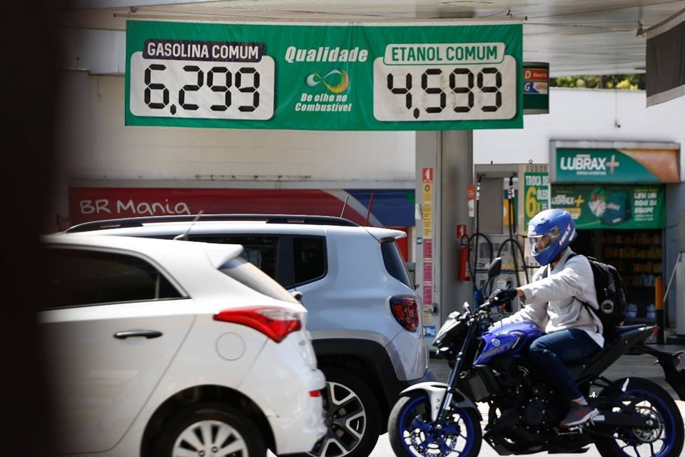 Imagem de posto de gasolina com tabela de preços da gasolina e do etanol. Carros e motos passam em frente ao posto - Metrópoles