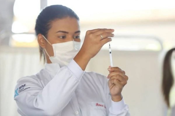 Mulher retirar com a seringa líquido contendo vacina contra a covid de recipiente