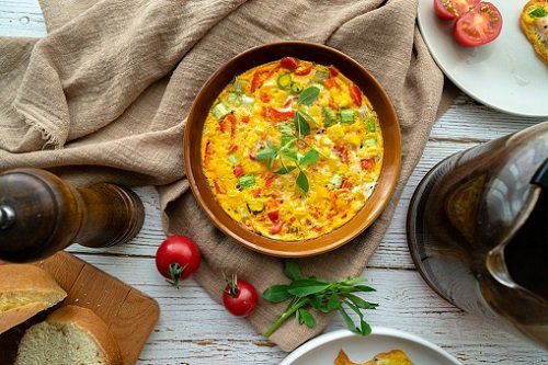 Fotografia mostra prato com omelete e tomates em cima de toalha de mesa marrom - Metrópoles