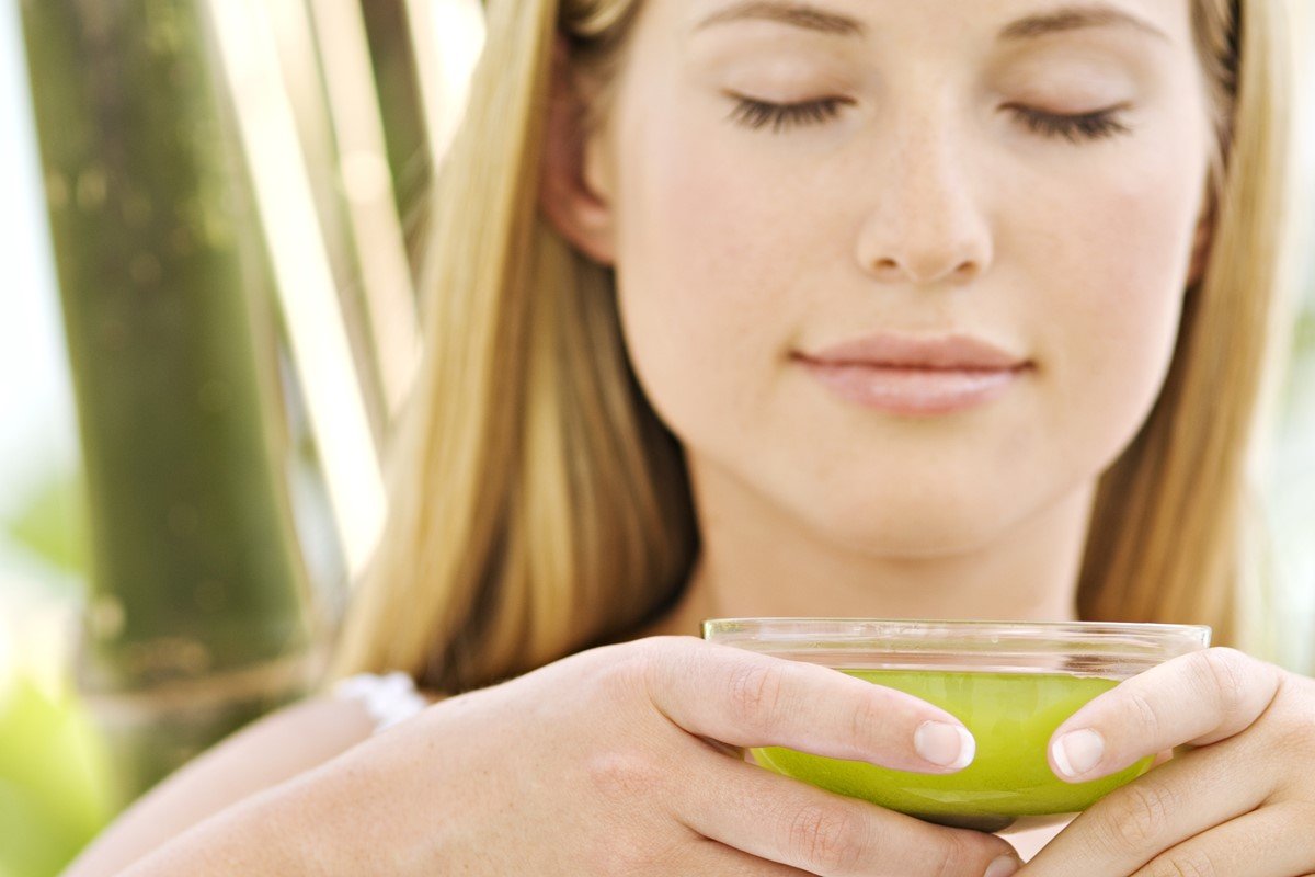 Foto colorida de uma mulher branca segurando uma taça de chá verde - Metrópoles