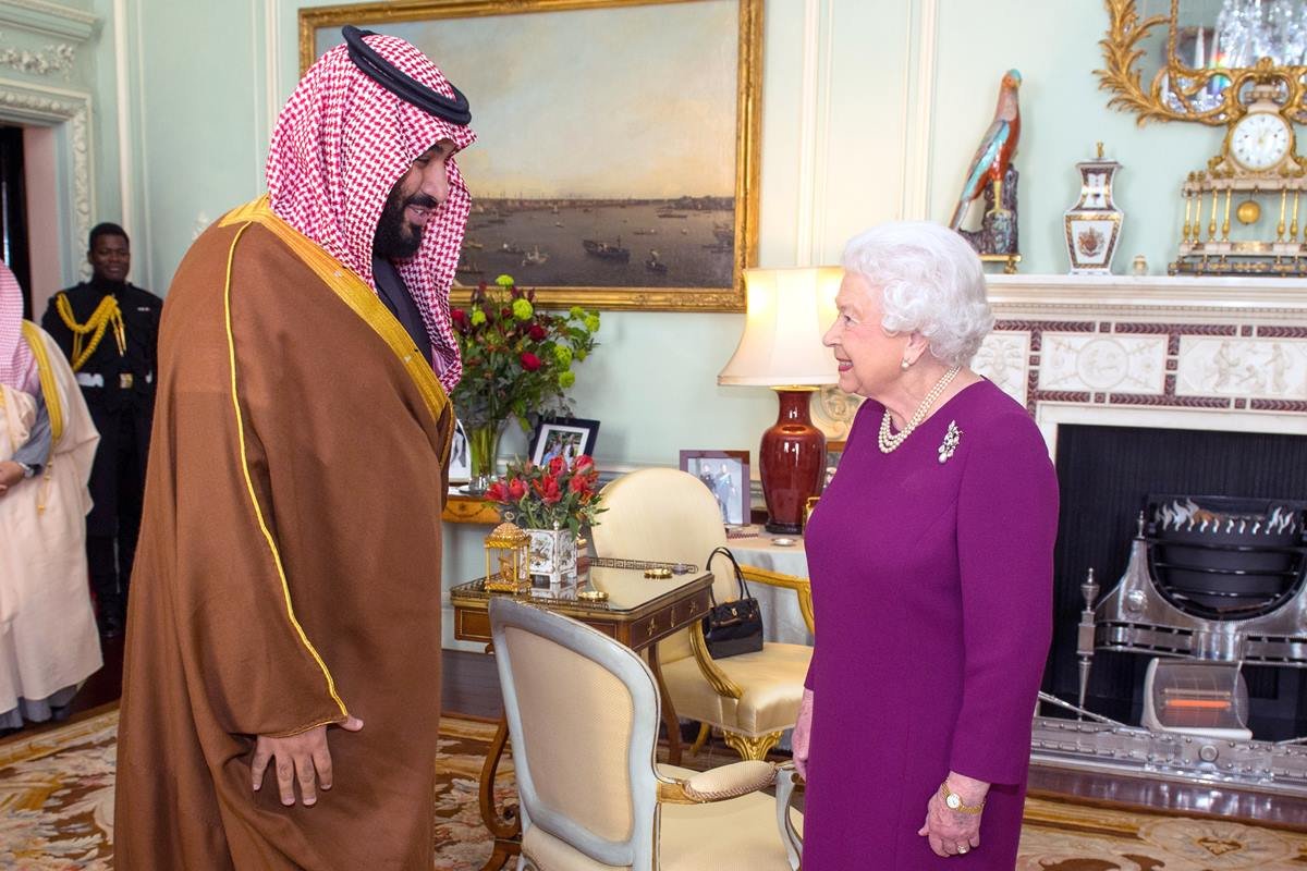 Foto colorida de homem pardo com vestes mulçumanas ao lado de mulher idosa, branca e com roupa violeta. Eles estão em uma sala luxuosa - Metrópoles