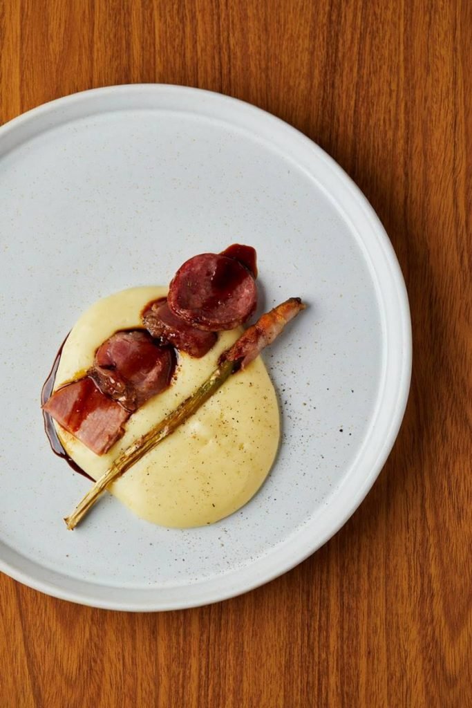 Picanha de porco servida na cama de aligot de mandioca acompanhado de aspargos com bacon