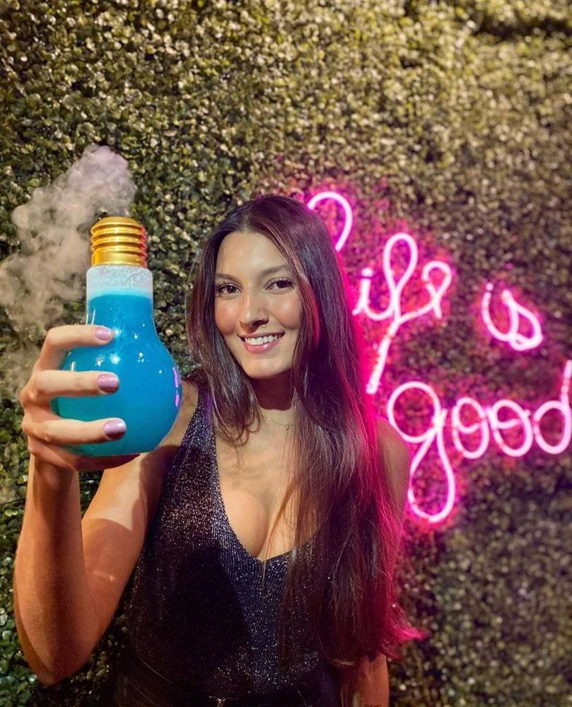 Na foto, uma mulher posa para a câmera com um drinque em formato de lâmpada - Metrópoles