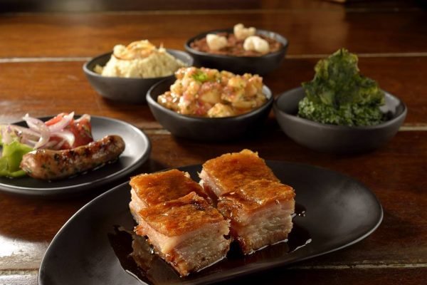 Na foto, diversos pratos feitos com carne de porco em uma mesa de madeira