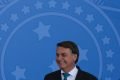 Presidente Jair Bolsonaro rindo; Ao fundo, escudo redondo azul-celeste, símbolo da república
