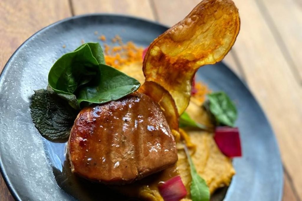 lombo de porco duroc ao molho demi glace com purê defumado de abóbora, picles de cebola roxa e pancs