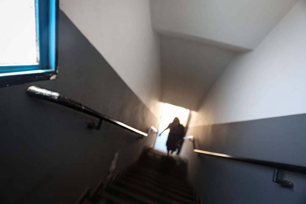 Corredor com uma escada e ao fundo uma pessoa subindo os degraus