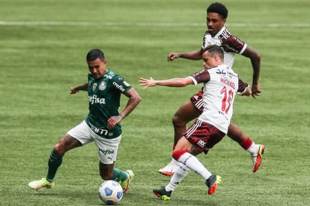 O atacante Dudu, do Palmeiras, corre com a bola enquanto é observado por dois jogadores do Flamengo