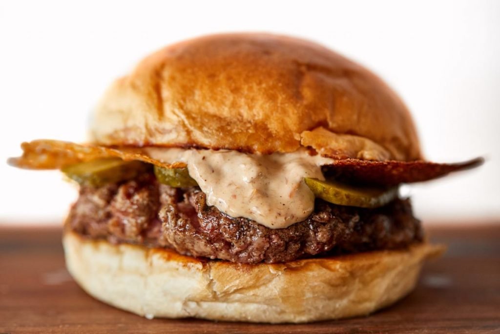 hamburguer com rapa de requeijao, carne, picles e molho escorrendo