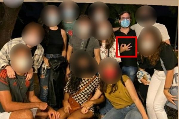 Grupo com rosto desfocado e um deles, de preto e de óculos, fazendo gesto de ok