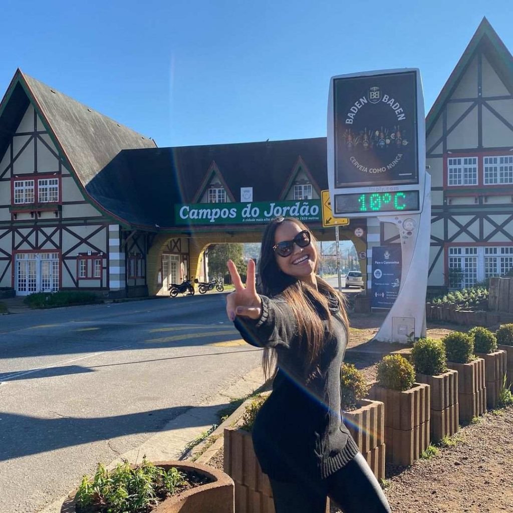 Mulher faz sinal da vitória em frente a placa de Campos do Jordão