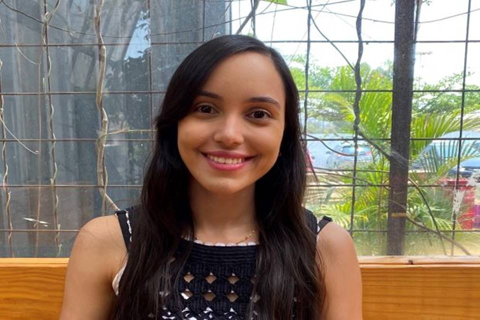 Menina de batom rosa e blusa preta sorrindo para a foto