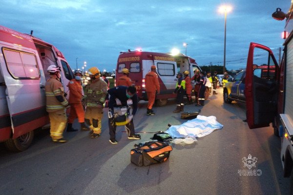 corpo coberto por pano deitado em asfalto com viaturas da polícia ao lado