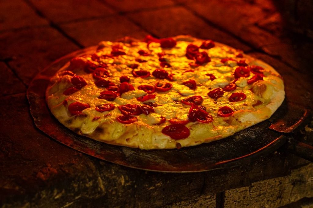na fotografia, forno a lenha com uma pizza com queijo e tomatinhos
