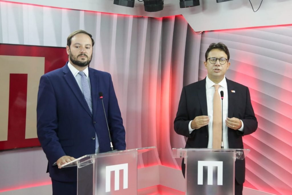 Dois homens de terno falando ao microfone