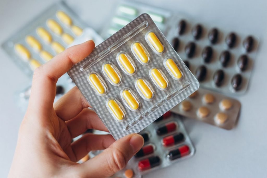 Fotografia colorida de mão segurando cartela de pílulas de remédio amarelas