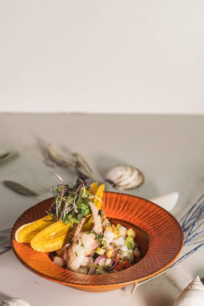 Na foto, cubos de peixe branco em um prato laranja com fundo bege