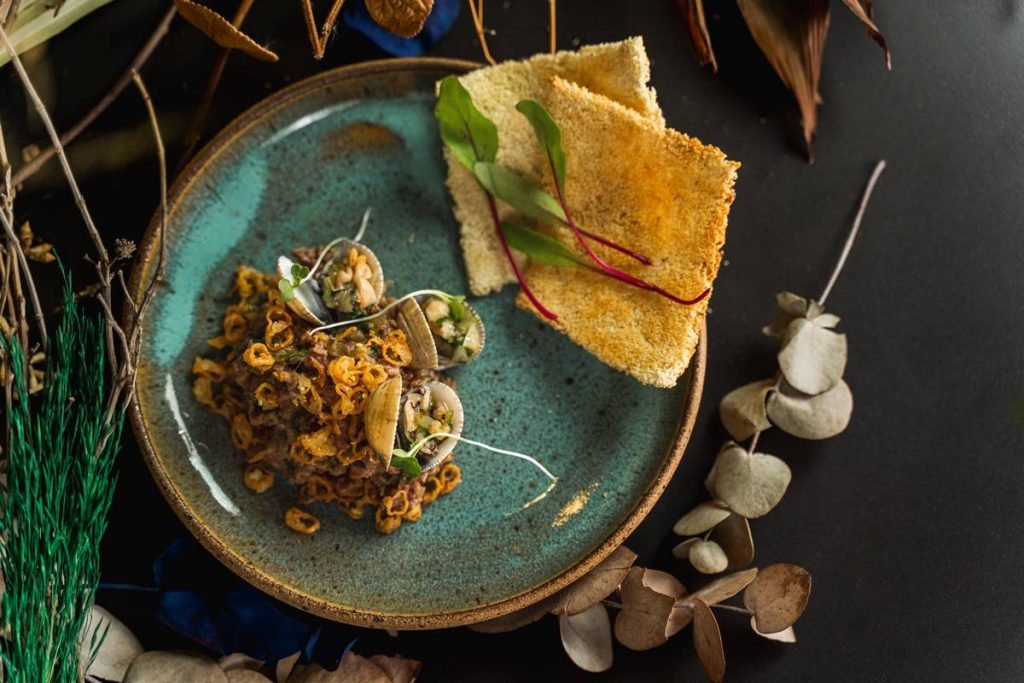Na foto, carne crua picada com tripas fritas em um prato azul com fundo preto