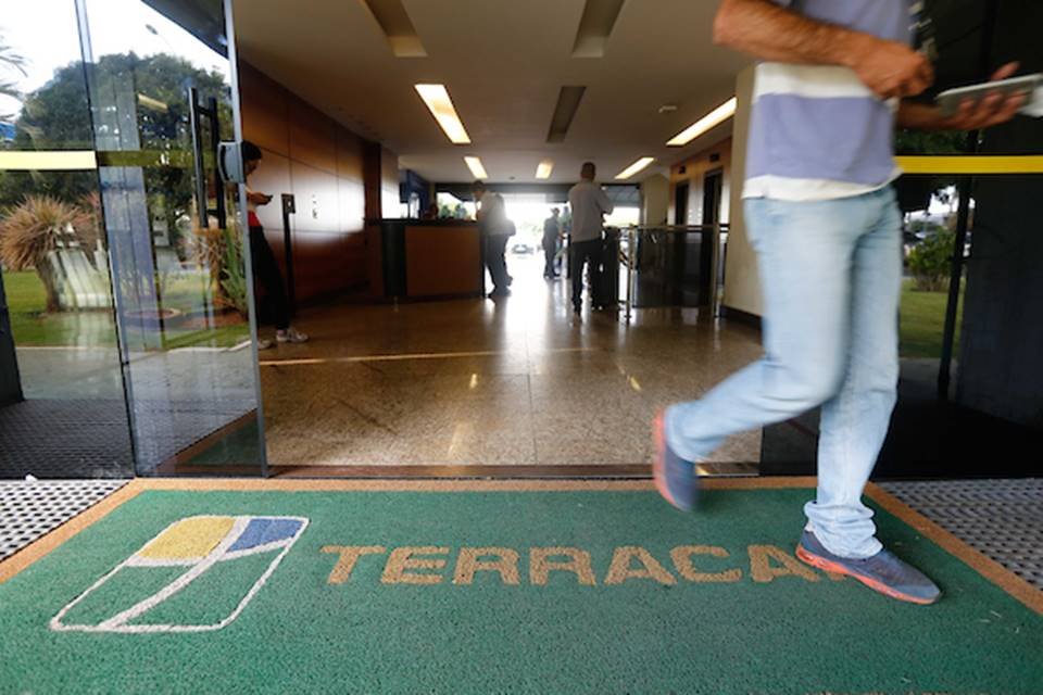 Um tapete verde com o logo da terracap e um homem pisando neste tapete, ele está de calça jeans