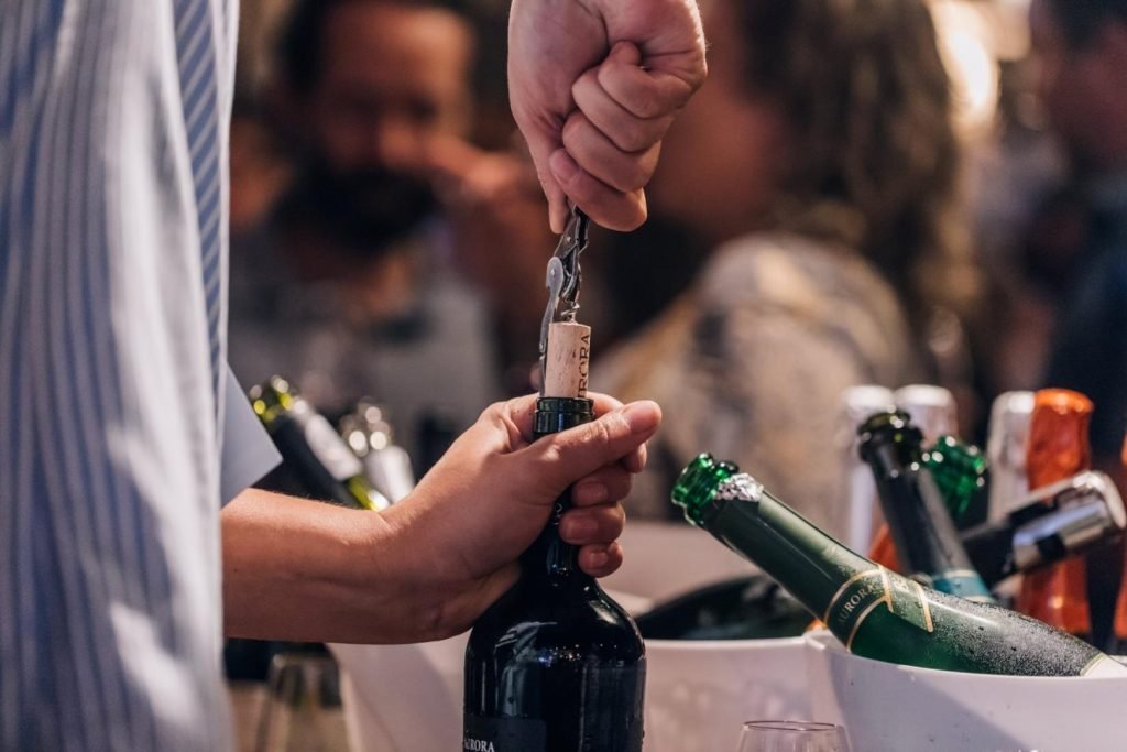 Na foto, uma pessoa abre uma garrafa de vinho