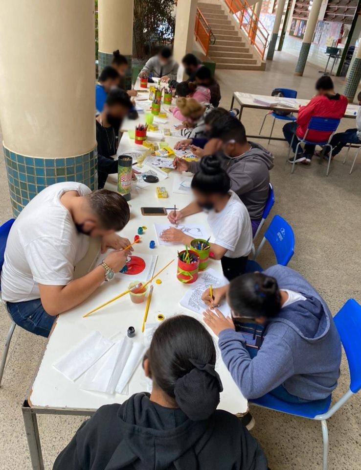 Alunos sentados em mesa e fazendo trabalho de arte