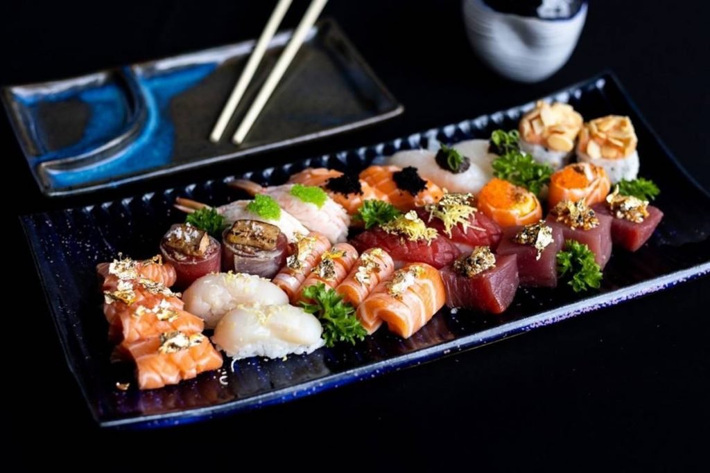 Na foto vemos um prato retangular com diversas peças de sushi e um hashi no canto superior direito da imagem