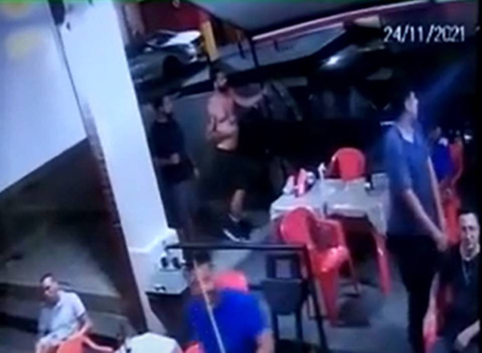 Homem sem camisa parado na porta do bar