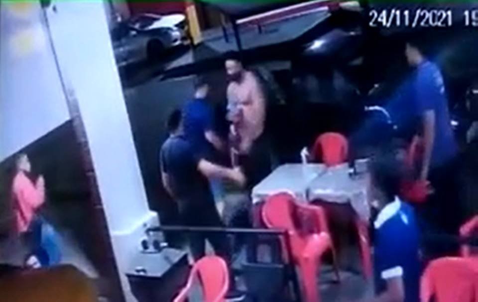 Homem de camisa azul entrega objeto a homem sem camisa