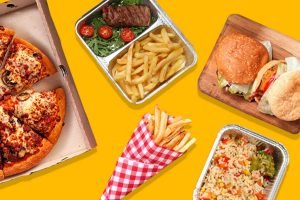 Na foto, vários tipos de comida com embalagens de delivery em um fundo branco. dentre as comifas, pizza, hambúrguer, arroz, batata frita, carne e salada