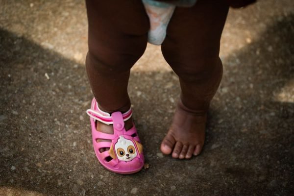 bebê usando fraudas e com apenas um sapato cor de rosa nos pés