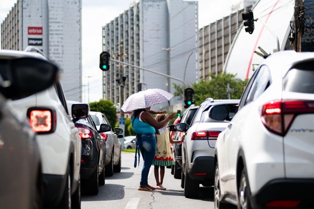 Mulher e criança utilizando um guarda-chuva em meio a carros