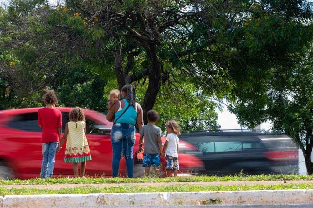Família parada ao lado de um carro vermelho em movimento