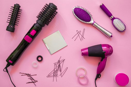 secadoras escovas e outros itens para cabelo em fundo rosa