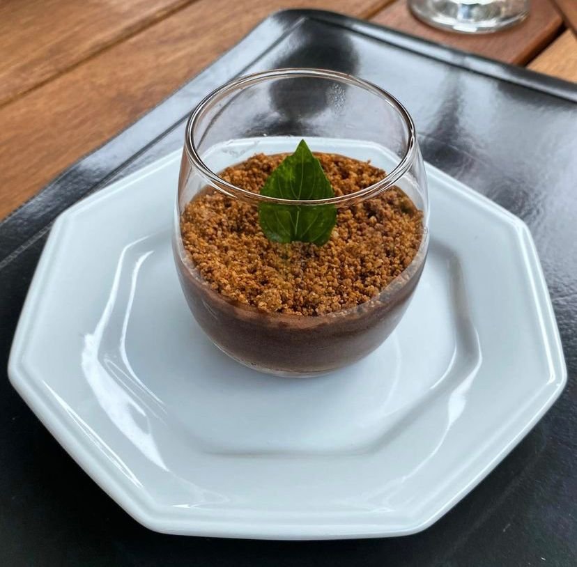 Na foto, um prato branco com um copo contendo Mousse de chocolate com crumble de castanha de caju