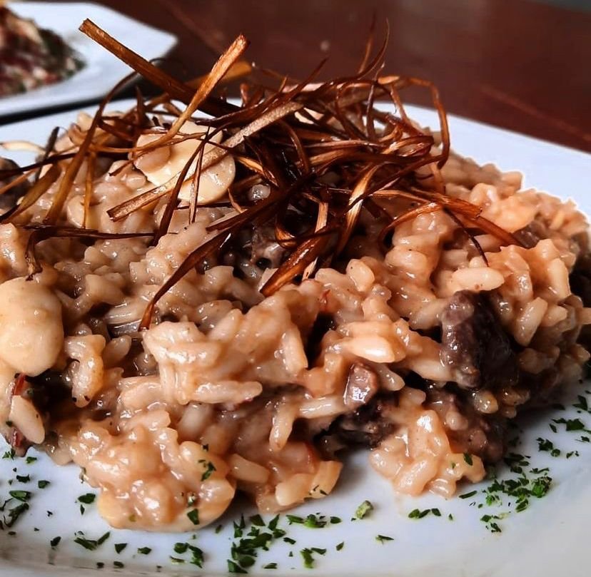 Na foto, um prato branco com Filé mignon ao molho de redução de vinho tinto com arroz à piamontese e crispy de batata doce