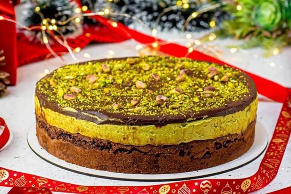 Na foto temos uma torta com base de brownie e camada de creme verde e decoração natalina ao fundo