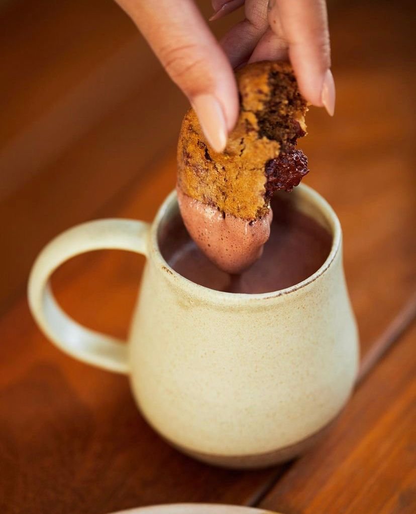 Na foto, um cookie mergulhando em uma xícada com chocolate quente