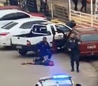 Homem no chão sendo detido por policiais militares de farda azul