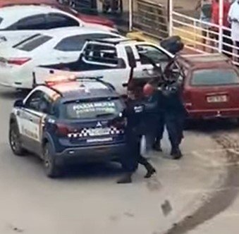 Homem no chão sendo detido por policiais militares de farda azul