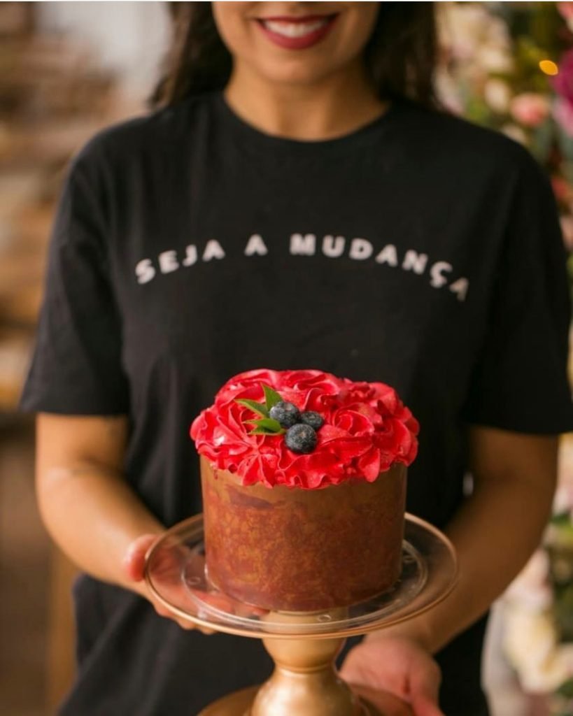 Na foto, uma mulher com blusa preta segura um panetone com cobertura vermelha