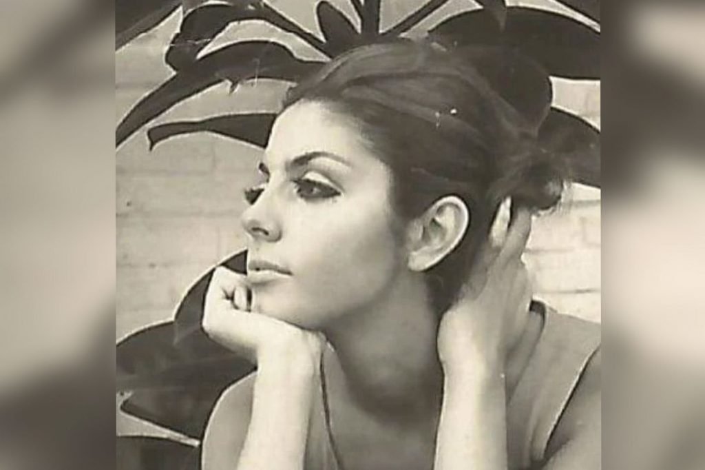 Na foto em preto e branco, Mila Moreira posiciona-se à direita enquanto olha para o lado esquerdo. Ela possui fisionomia séria e está com uma das mãos sobre o queixo enquanto a outra segura os cabelos presos. Ao fundo há folhas.